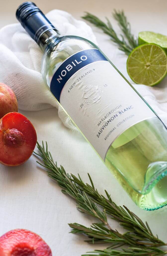 Sauvignon Blanc wine bottle with fresh limes, pomegranate, and rosemary for a refreshing vibe.